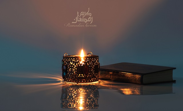 القرآن الكريم وإضاءة شمعة داخل فانوس تعبيرية عن موعد شهر رمضان