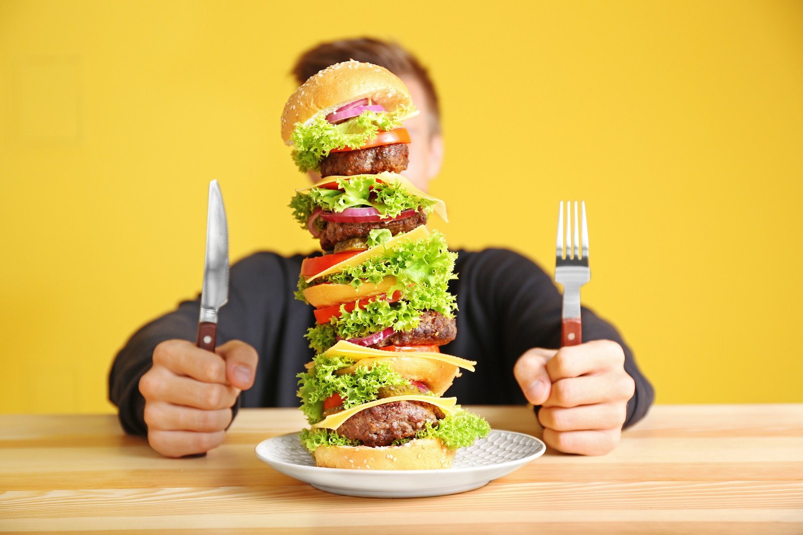 رجل يمسك شوكة أمامه طعام تعبيرية عن الوجبات السريعة - مصدر الصورة: Shutterstock