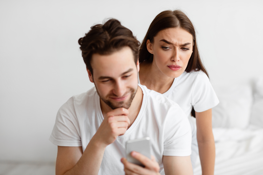 زوجة تنظر في هاتف زوجها - تعبيرية عن الغيرة بين الزوجين : shutterstock